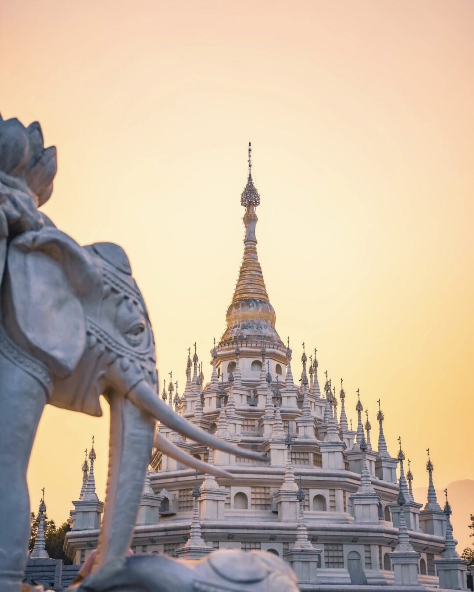 Gold and silver pagodas with elephant statues silhouetted against a Mangshi sunset — Yunnan slow culture tour