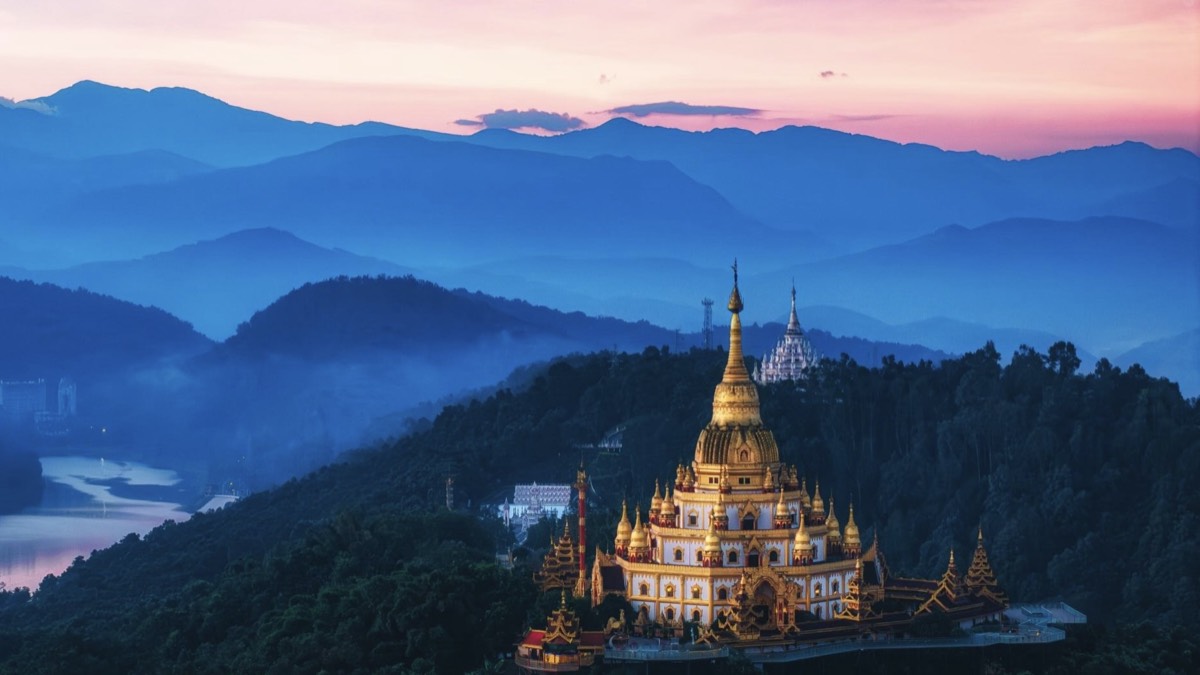 Mangshi's golden Menghuan Pagoda glowing at dusk over Yunnan's layered blue ridges — Yunnan slow culture tour