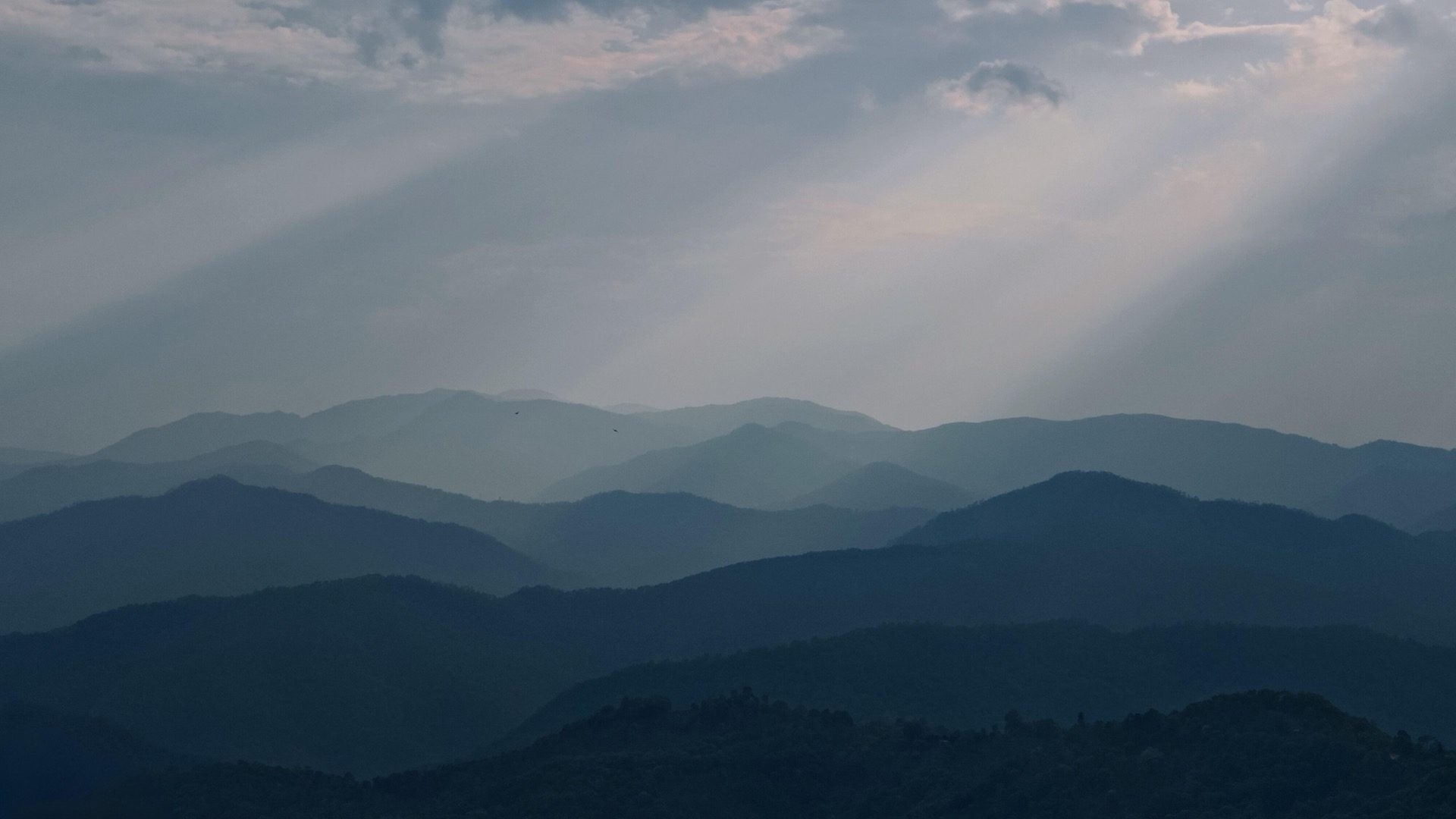 Layered misty mountain ridges with god-rays through the clouds over the Pu'er tea country — Hani-tended Nannuo, Xishuangbanna