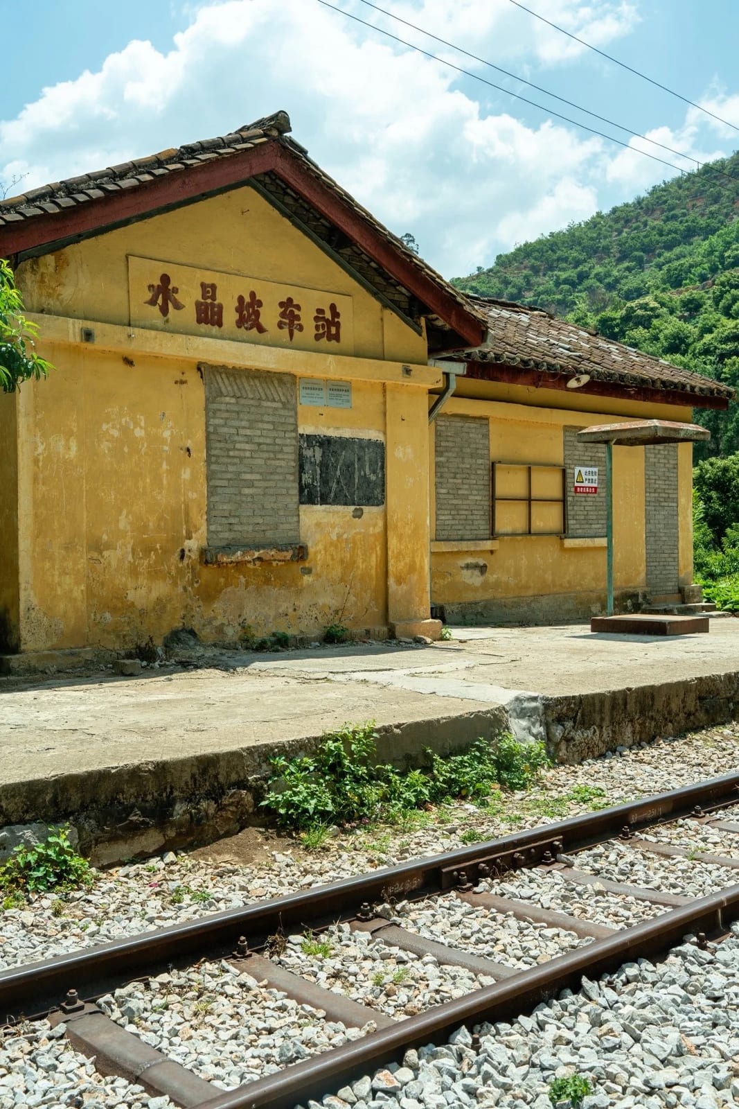 Shuijingpo station (水晶坡车站) on the Yunnan–Vietnam Railway — a yellow station house with its name on the wall and the track in front