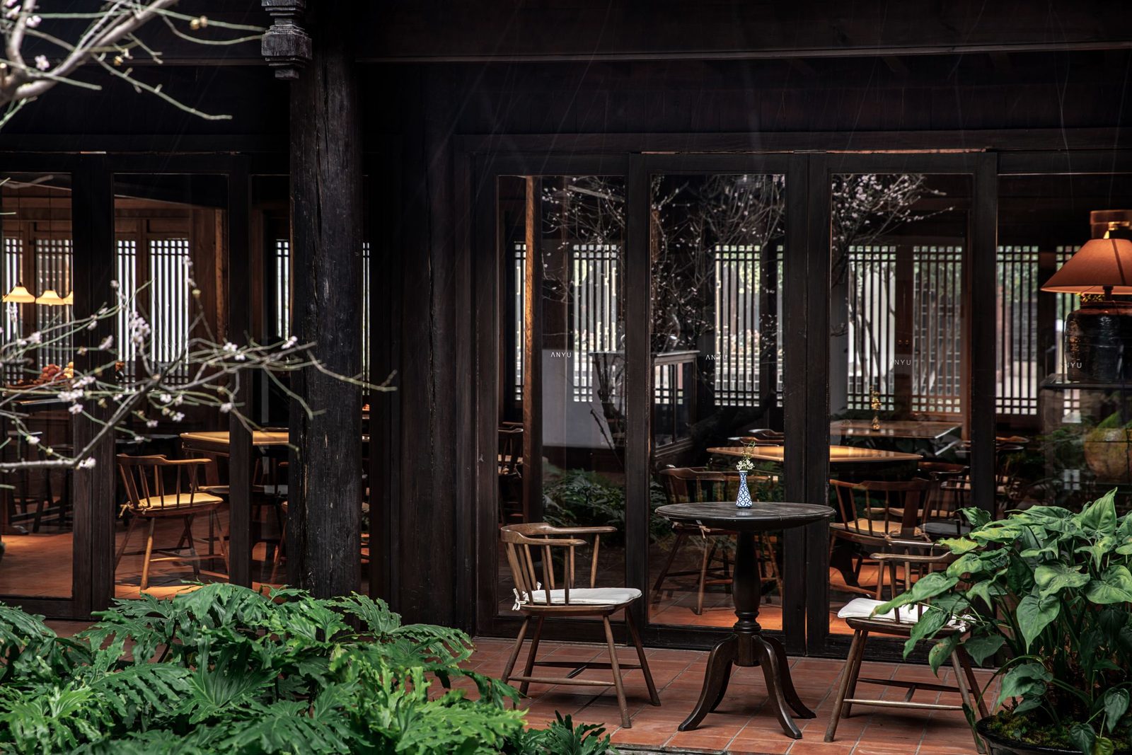 Lounge opening onto the courtyard through carved lattice doors, round tables and leafy plants in front.