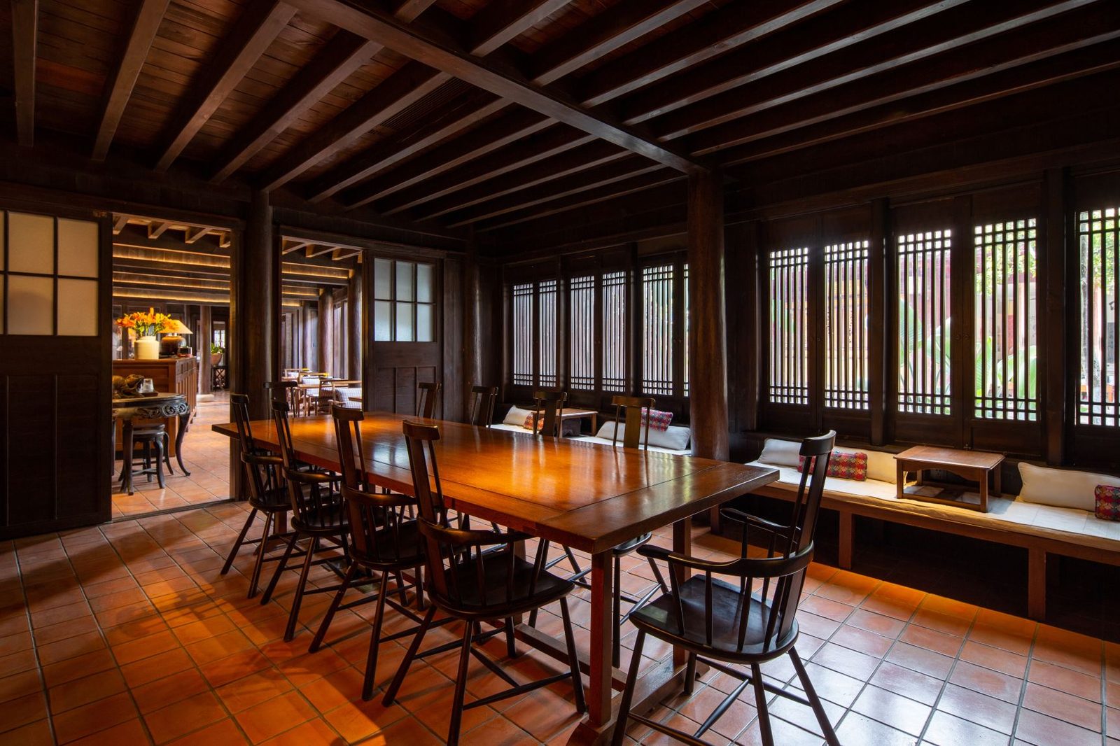Dining room with a long table and spindle-back chairs in dark timber, lattice windows along one side.