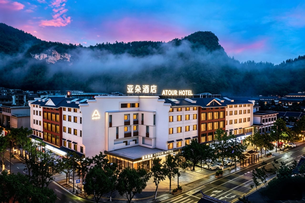 Atour Hotel, Zhangjiajie Forest Park Gate (张家界国家森林公园标志门亚朵酒店) — the hotel lit at dusk, mist over the forested mountain behind