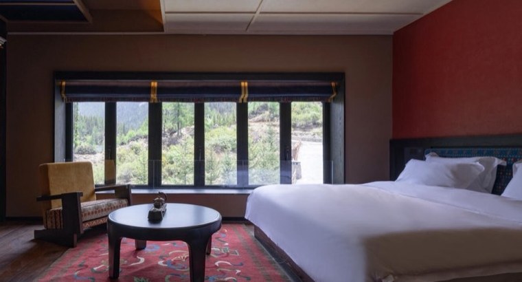 Bore Yading — a guest room with a red wall, a carved Tibetan cabinet and a picture window onto the larch forest