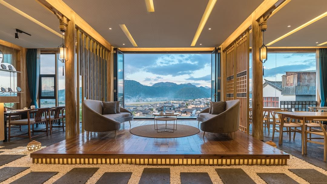 Boyun Hot Spring Inn — a lounge with tub chairs on a raised timber platform, folding glass doors open to Heshun's rooftops and the mountains beyond