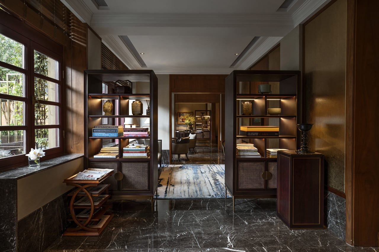 Capella Shanghai, Jian Ye Li — a lounge lined with open bookshelves, dark marble floors and a sitting room beyond