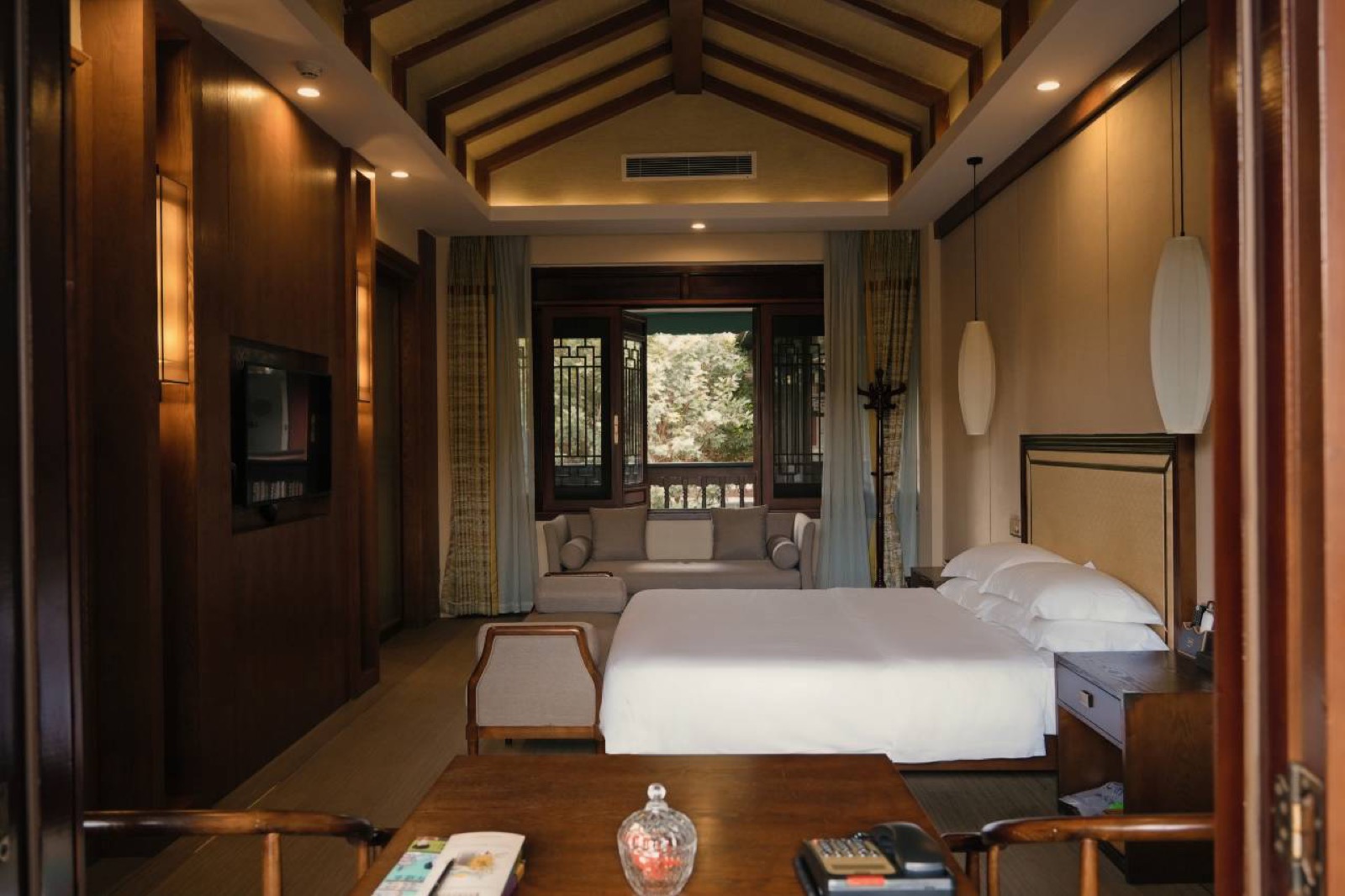 Hanlinyuan Courtyard — guest room under a pitched beamed ceiling with dark-wood panelling and latticed windows onto the garden