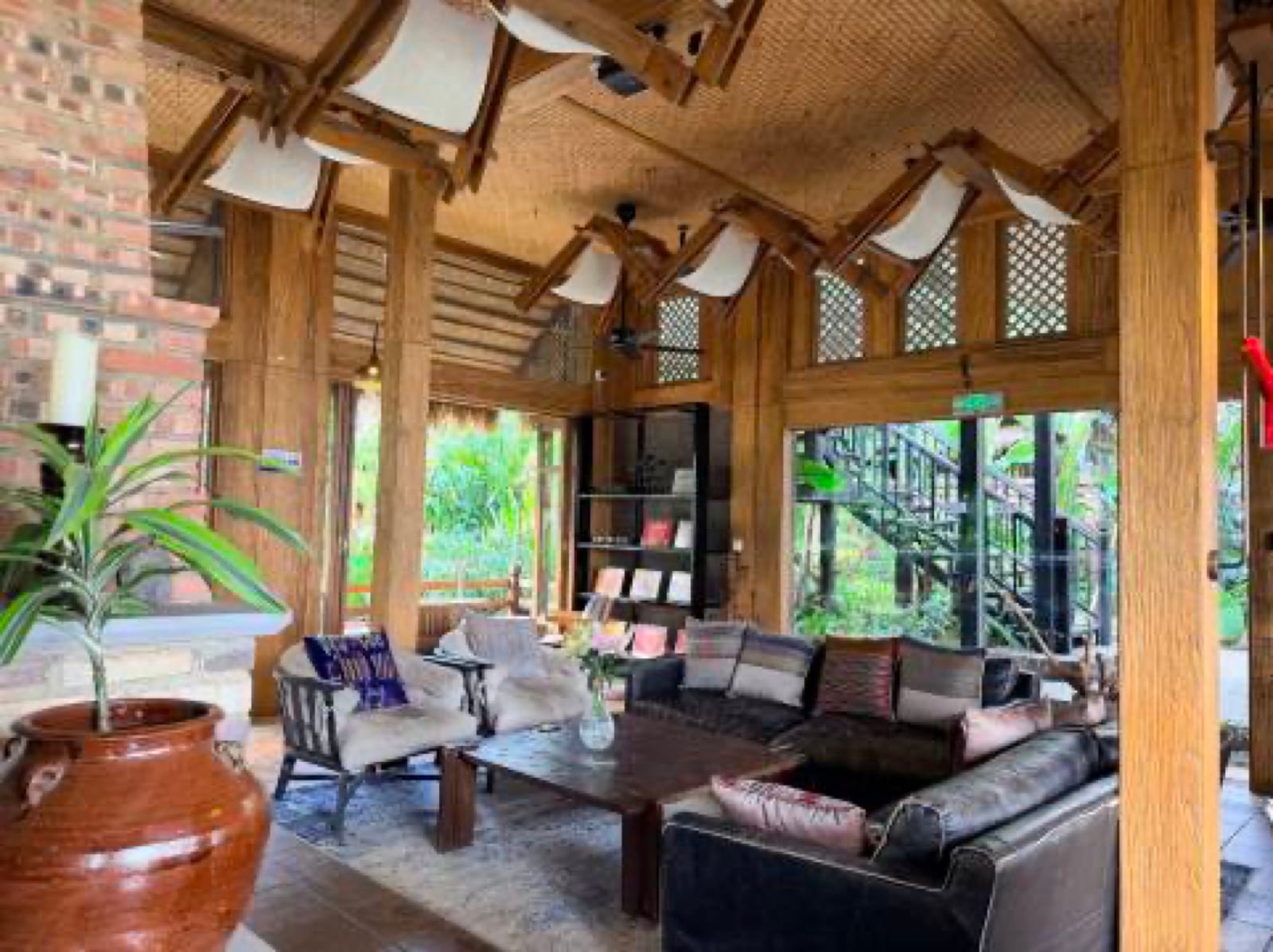 Huke Coffee Manor — the open-sided timber lounge under a woven-bamboo roof, leather sofas and a large earthen jar, glass walls opening to the forest above the Nujiang valley