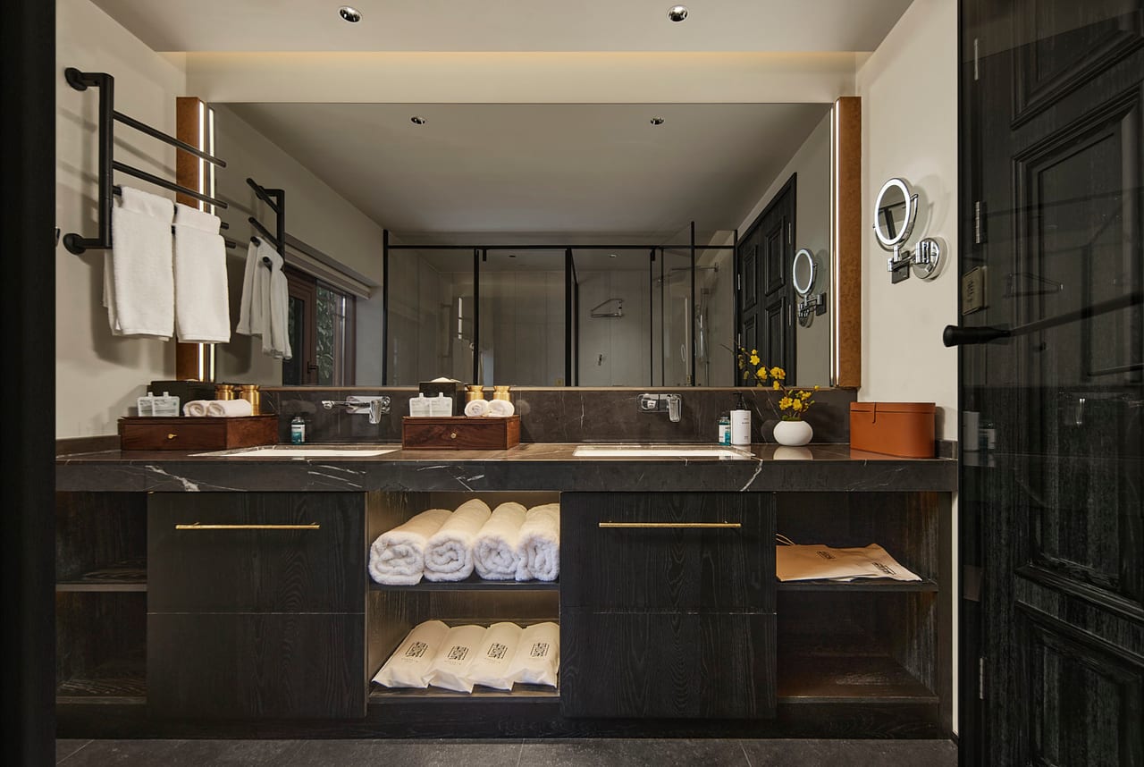 Kogongdi — dark-stone bathroom with open shelving and folded linen