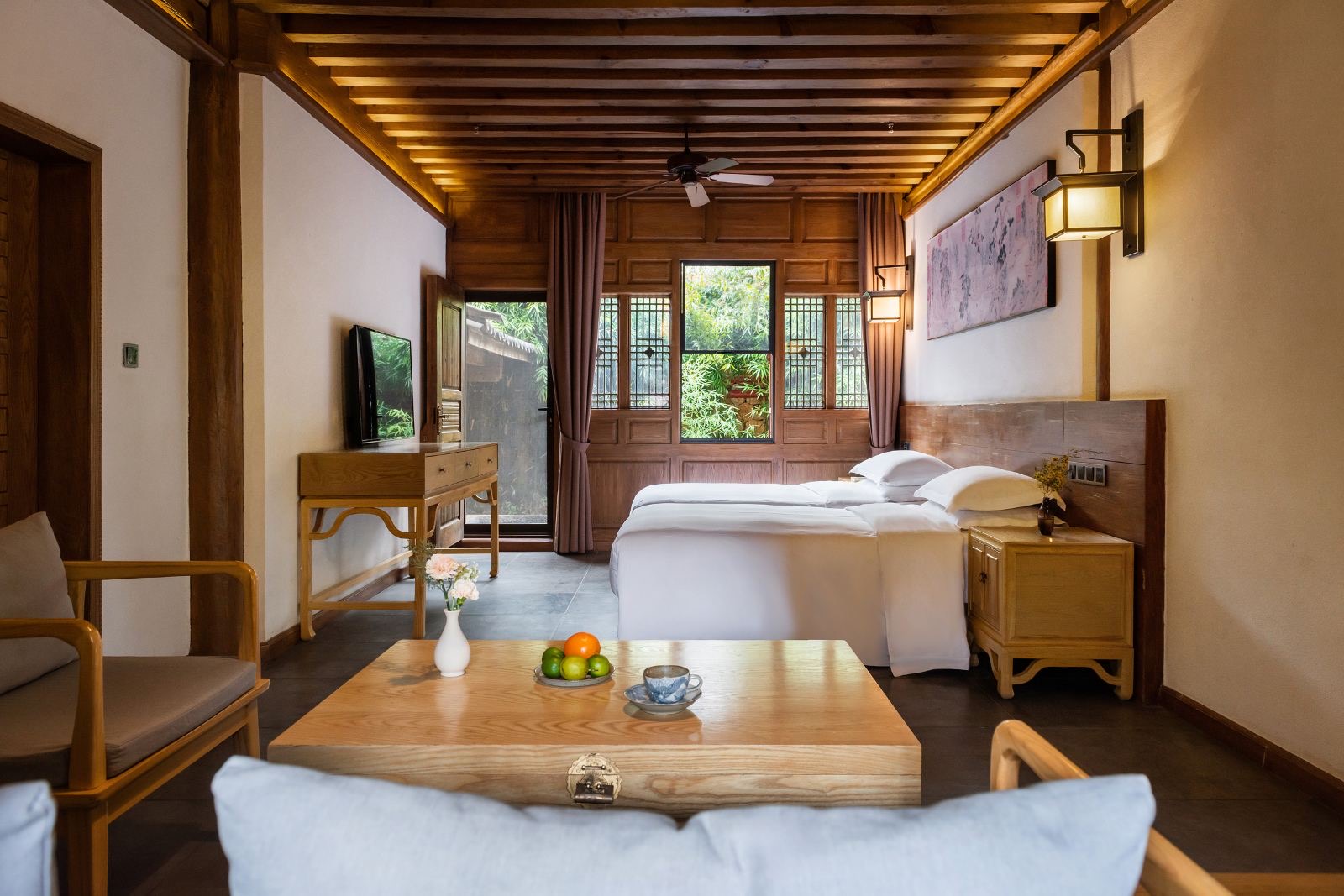 Lanlinge — a timber-beamed guest room with plain wood furniture and lattice windows opening onto bamboo, a landscape scroll above the beds
