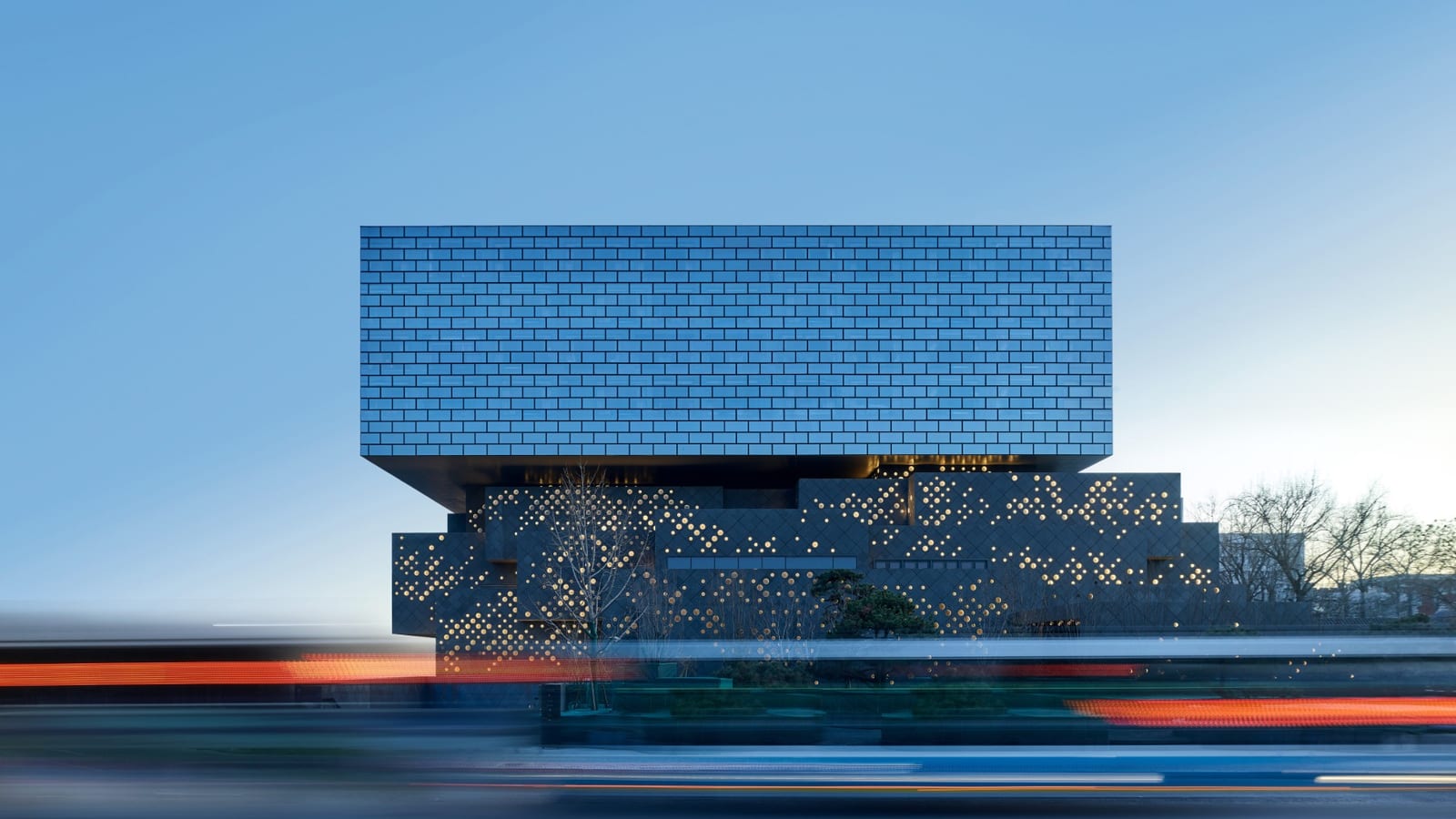 The PuXuan Hotel and Spa, Beijing (北京璞瑄酒店) — the Guardian Art Center building at dusk, a brick-patterned glass block above a lit, perforated base