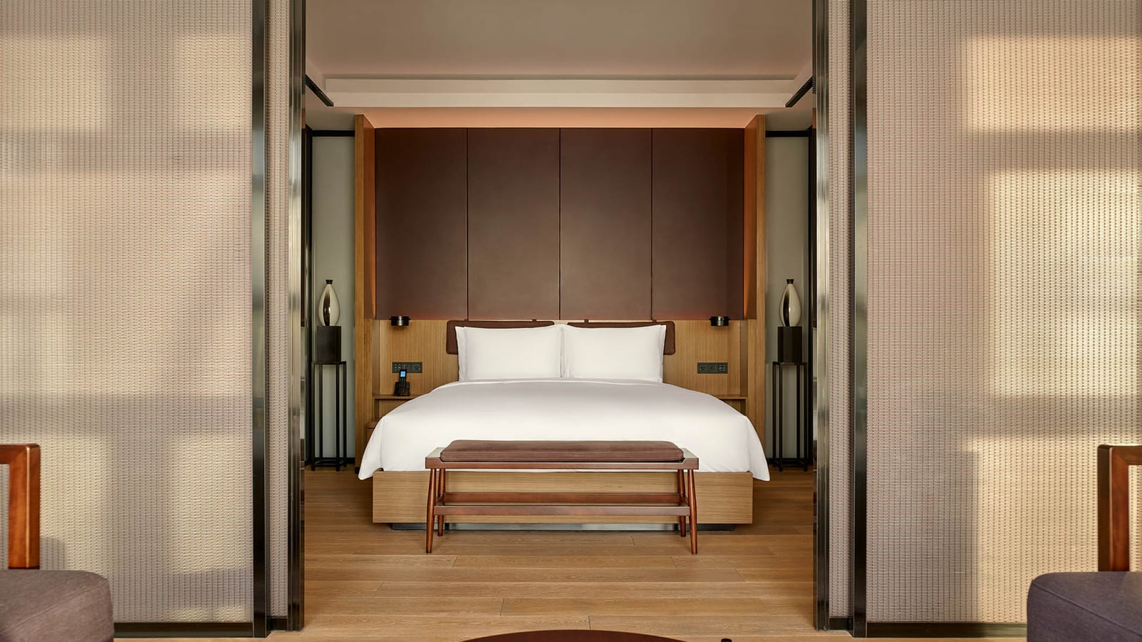 The PuXuan Hotel and Spa, Beijing — a suite bedroom seen through open sliding screens, a king bed against timber and brown wall panels