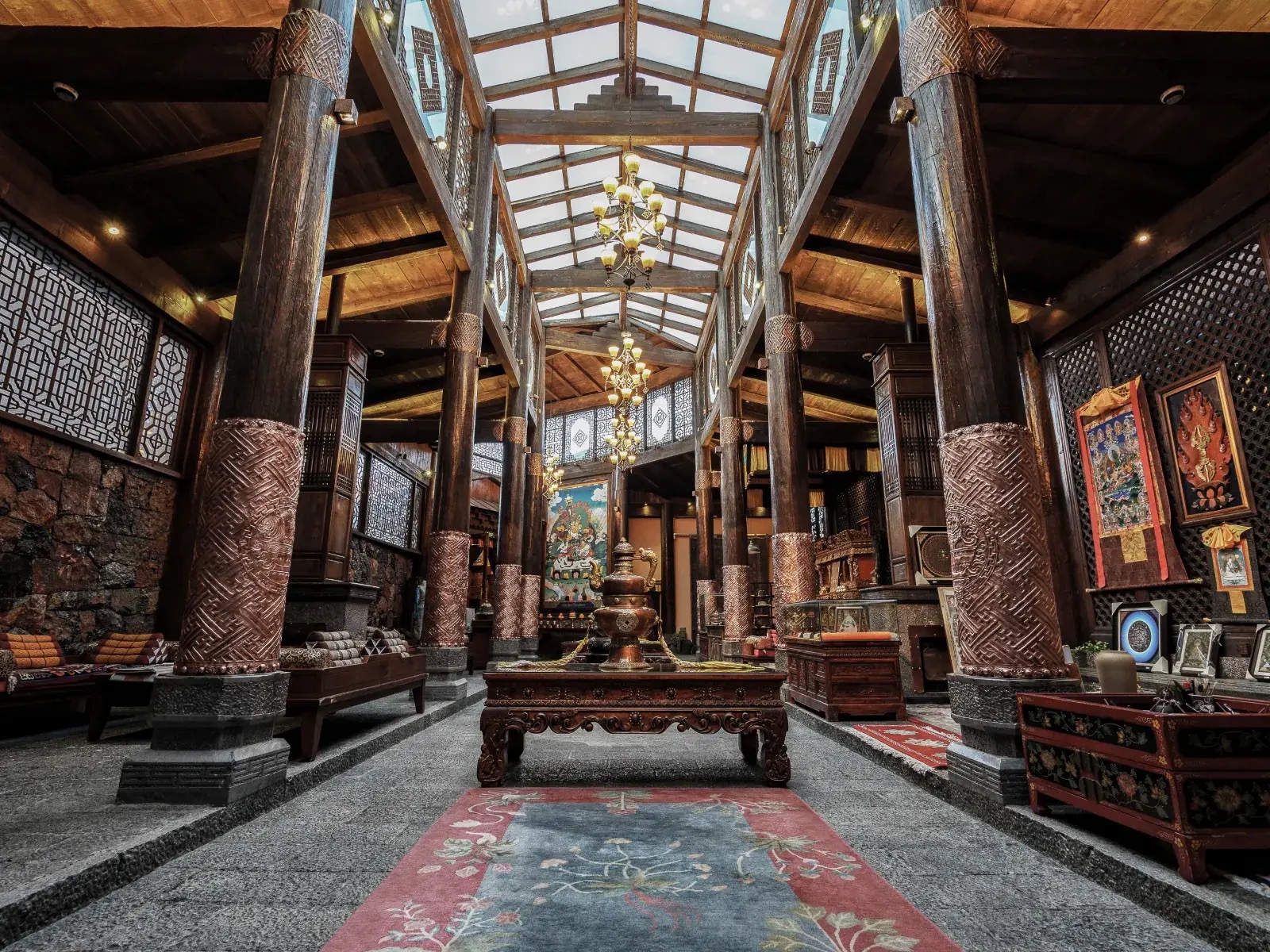 Sangzhu Bieyuan — the skylit timber hall on massive carved copper-clad pillars, thangkas along the wall and a bronze urn on the central table