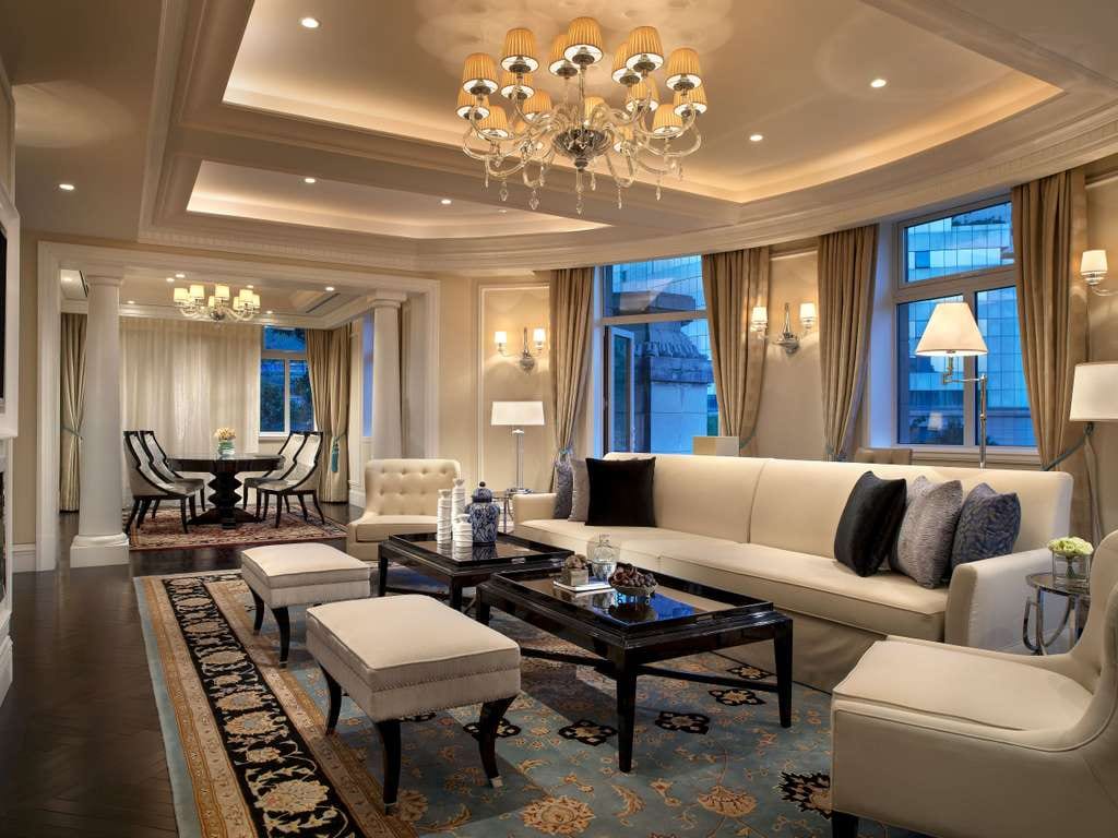 Sofitel Legend People's Grand Xi'an — a suite's long living room under a crystal chandelier, a cream sofa and black lacquer tables on a blue patterned rug, a round dining table beyond white columns