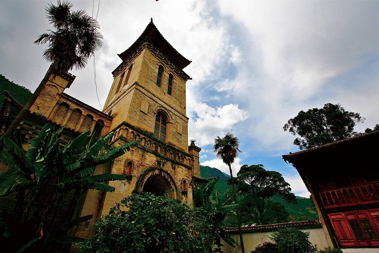 Songtsam Lodge Cizhong — the bell tower of Cizhong's French mission church rising above palms and a Tibetan house with painted eaves
