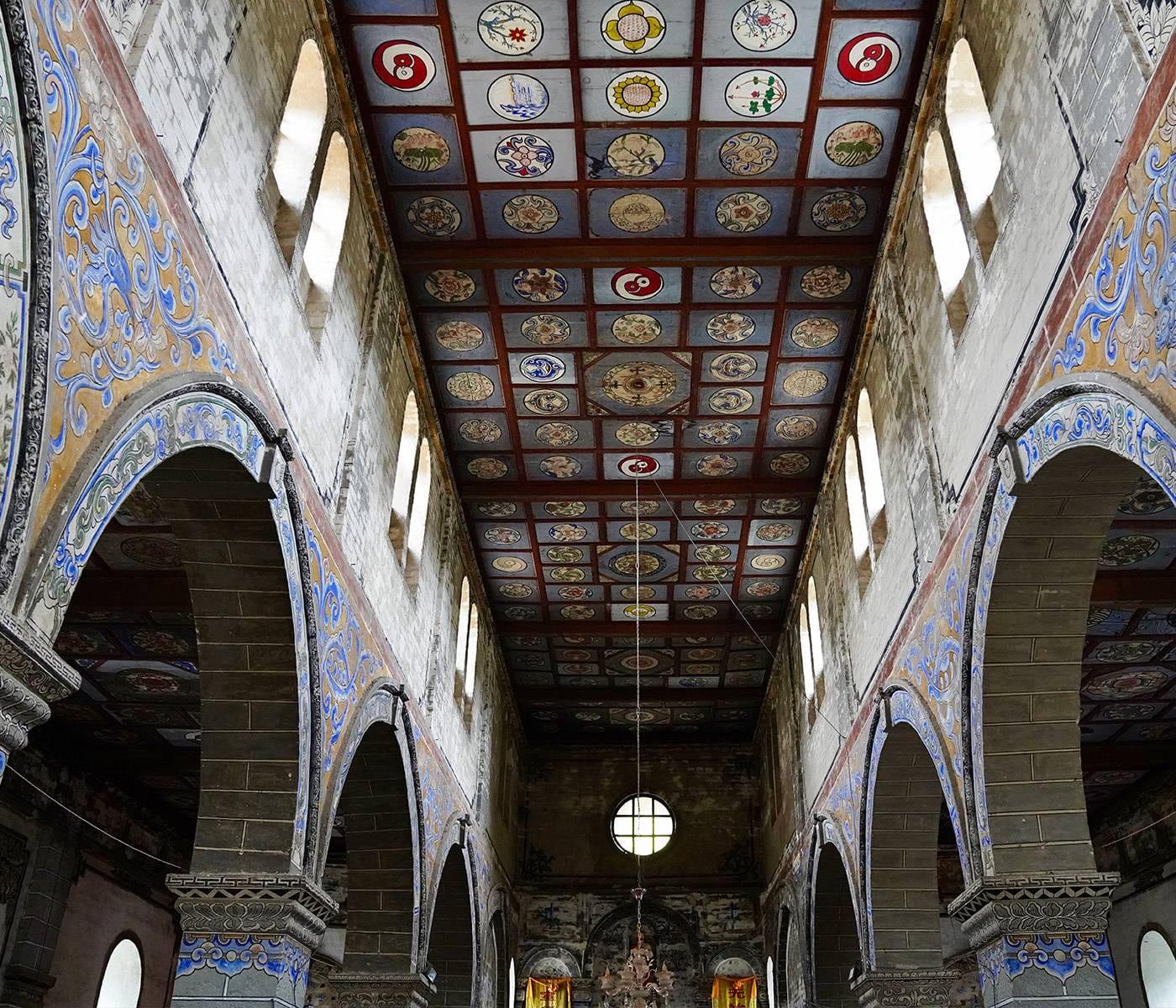 Songtsam Lodge Cizhong — inside Cizhong church, round stone arches and a ceiling painted with Chinese and Tibetan motifs above the nave