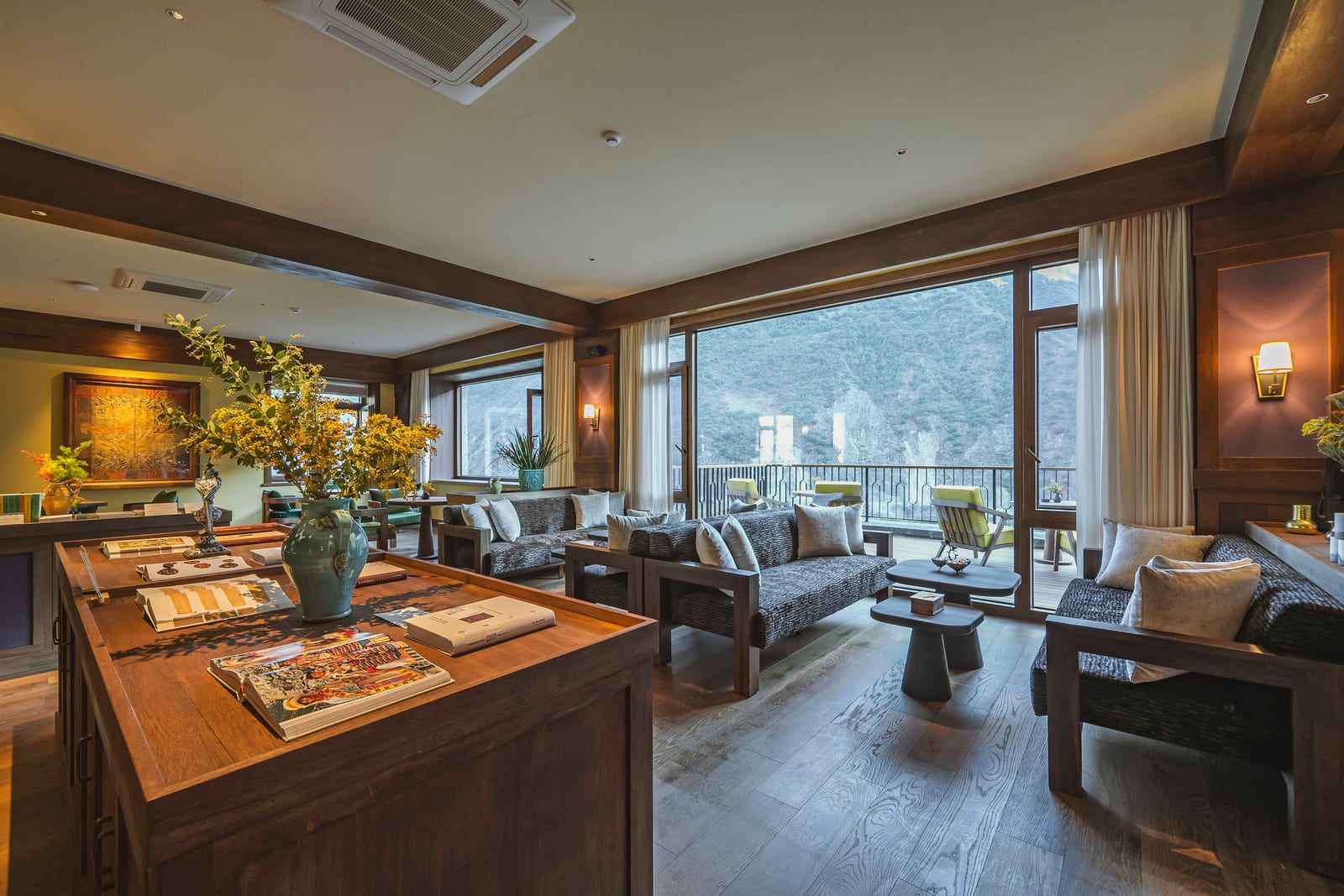 Songtsam Lodge Cizhong — the lobby lounge, sofas and a timber display table with flowers and books in front of full-height windows onto the valley