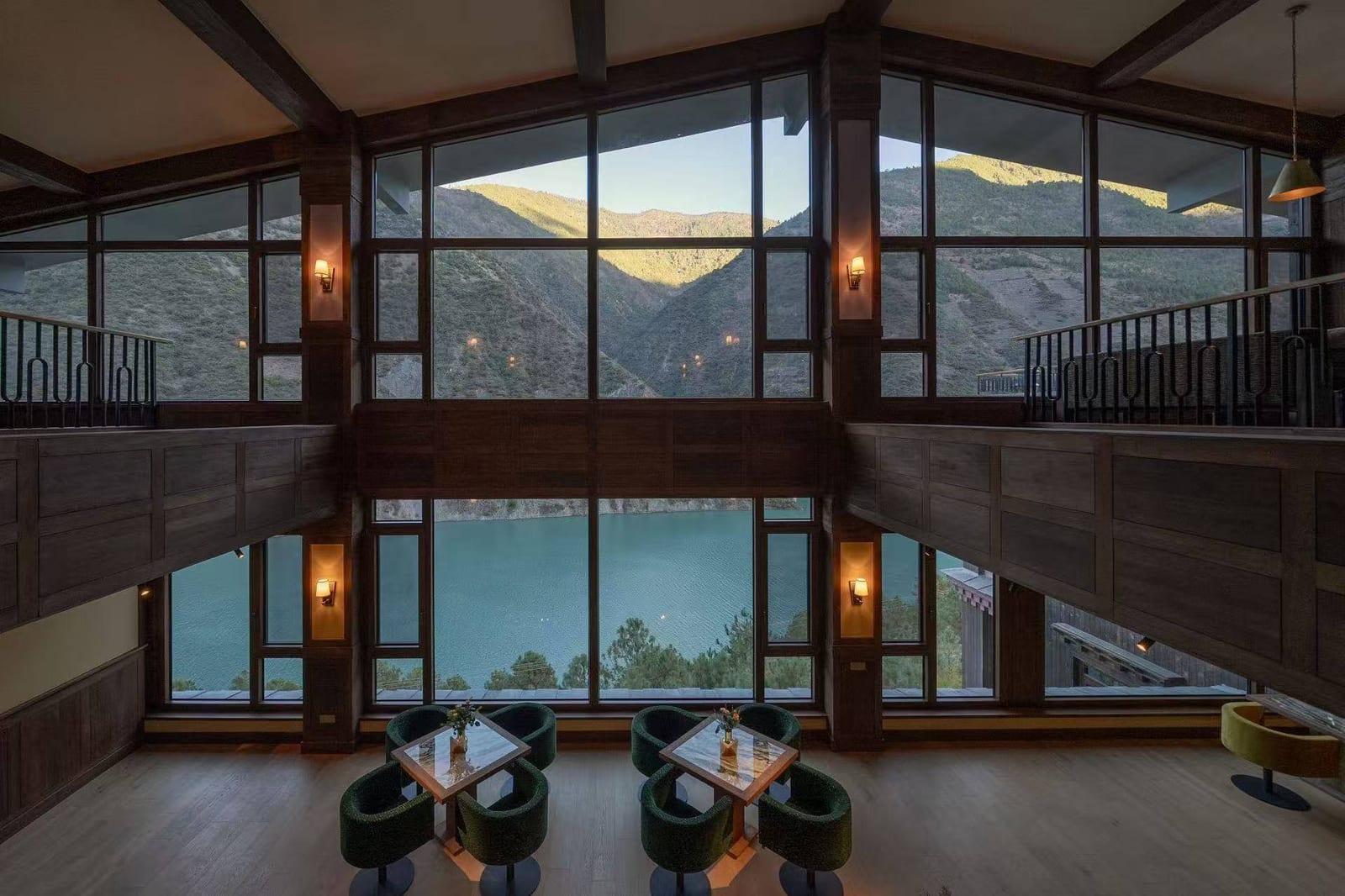 Songtsam Lodge Cizhong — a lounge with a double-height glass wall framing the turquoise river below and the far slopes of the gorge, armchairs set at low tables