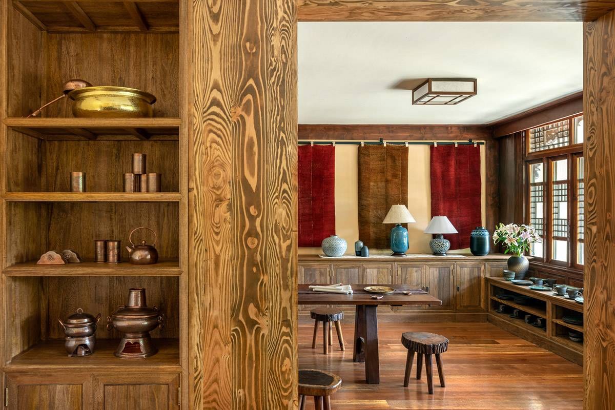 Songtsam Lodge Shangri-La — a dining room seen past shelves of copper pots and kettles, red and brown woven hangings above blue glazed jars, and rustic stools at a long wooden table
