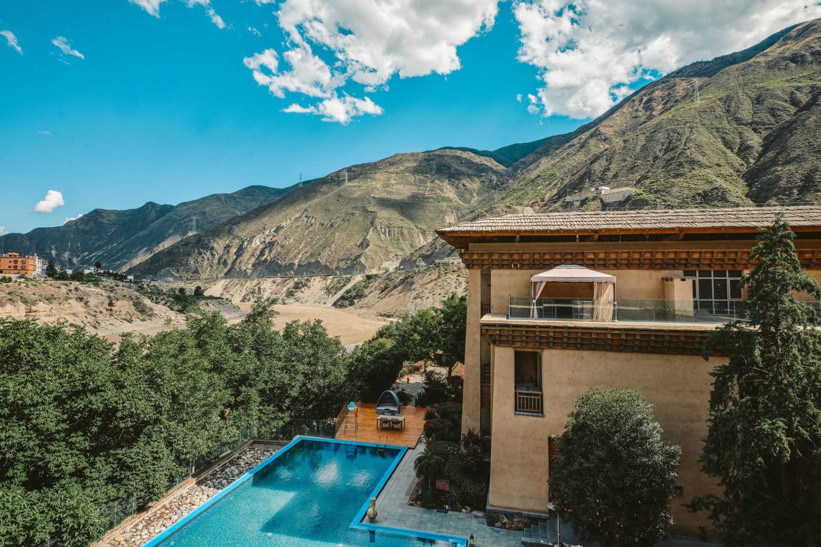Tea Horse Road Benzilan — the lodge from above, its rammed-earth blocks and terraces among trees with a pool in the garden, the bare hills of the Jinsha valley behind