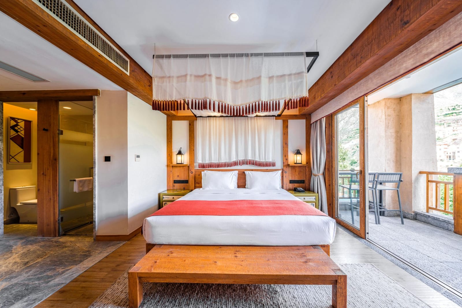 Tea Horse Road Benzilan — a king room under timber beams, the bed beneath a slatted canopy and glass doors open to a balcony