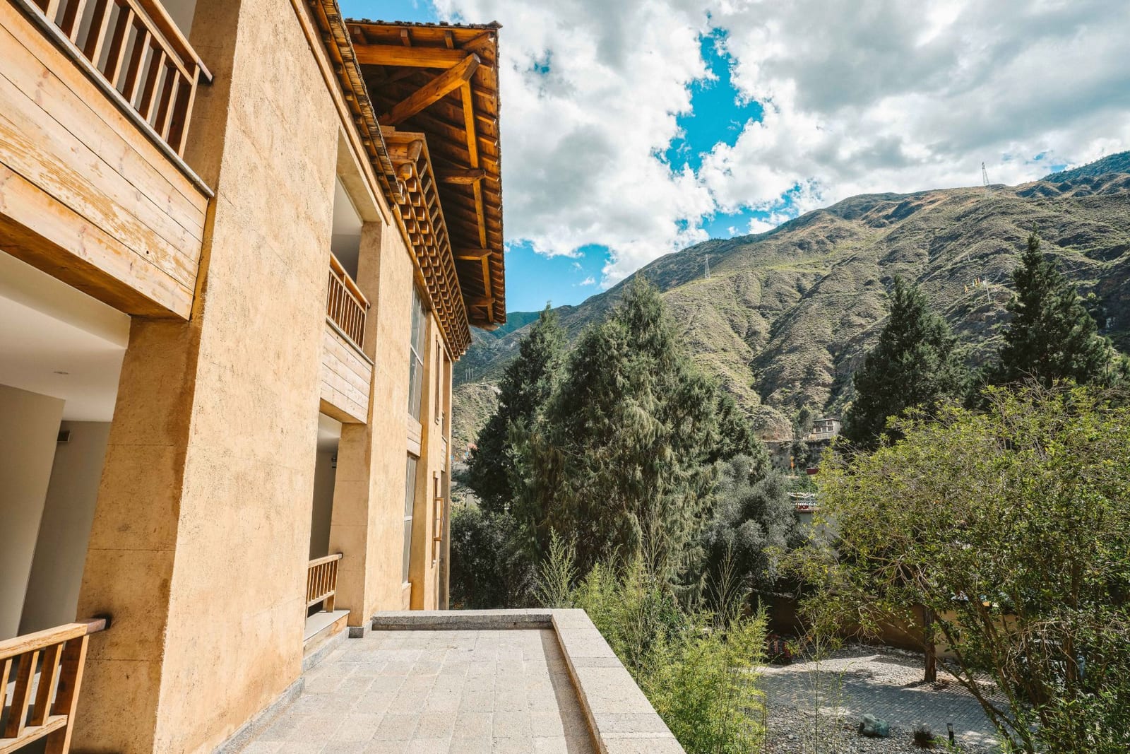 Tea Horse Road Benzilan — a stone terrace along the rammed-earth wall of the lodge, timber balconies above and the dry hills of the Jinsha valley beyond