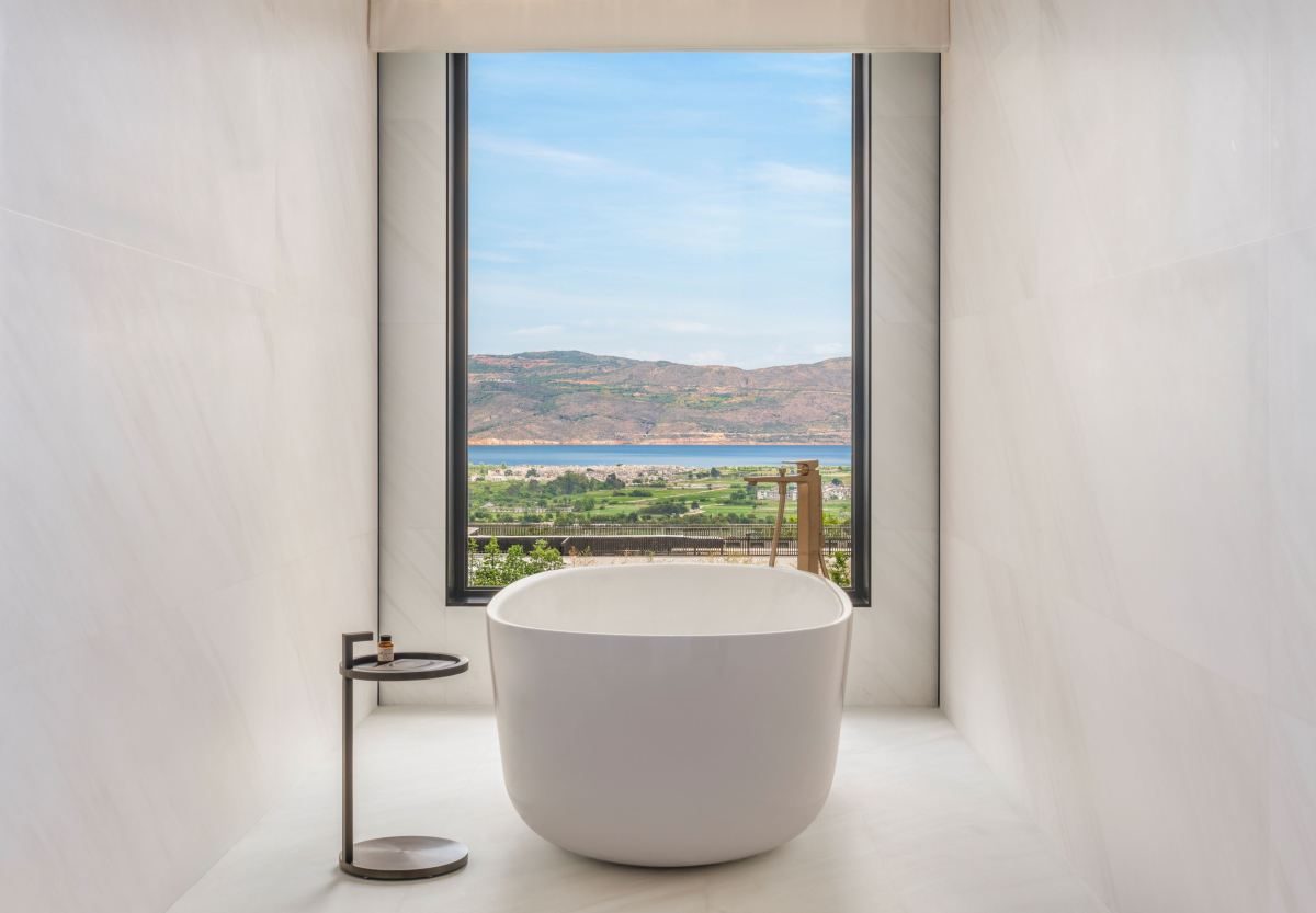 Freestanding bathtub in a pale stone bathroom, a tall window looking down to Erhai Lake.