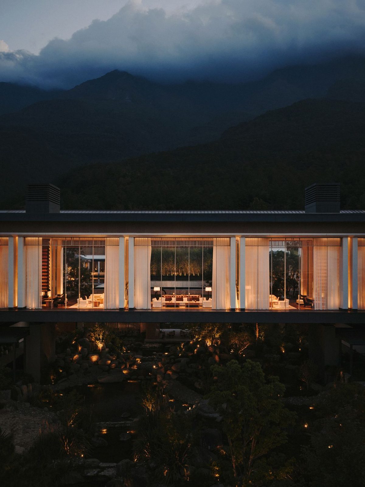 The glass-walled lounge glowing at night beneath the dark ridge of Cangshan.