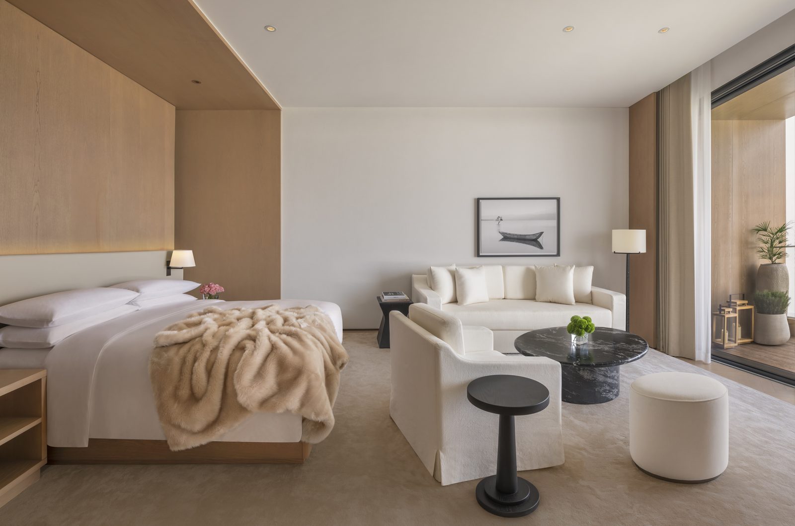 Lake-view king room with a timber bed wall, a faux-fur throw and a sitting area by the balcony doors.