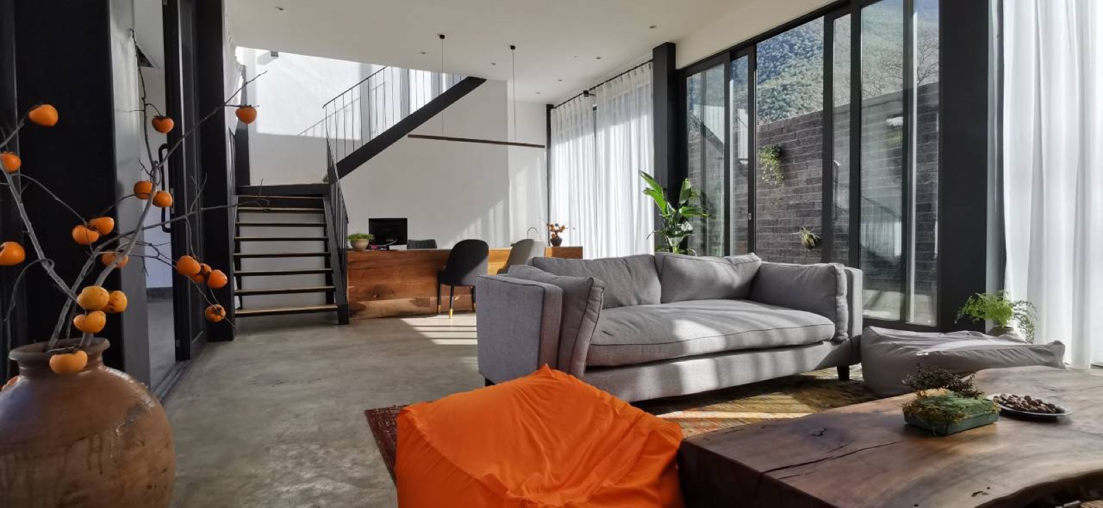Tianyu Tacheng — double-height lounge in raw timber and glass, live-edge table and grey sofa facing the forested valley slopes