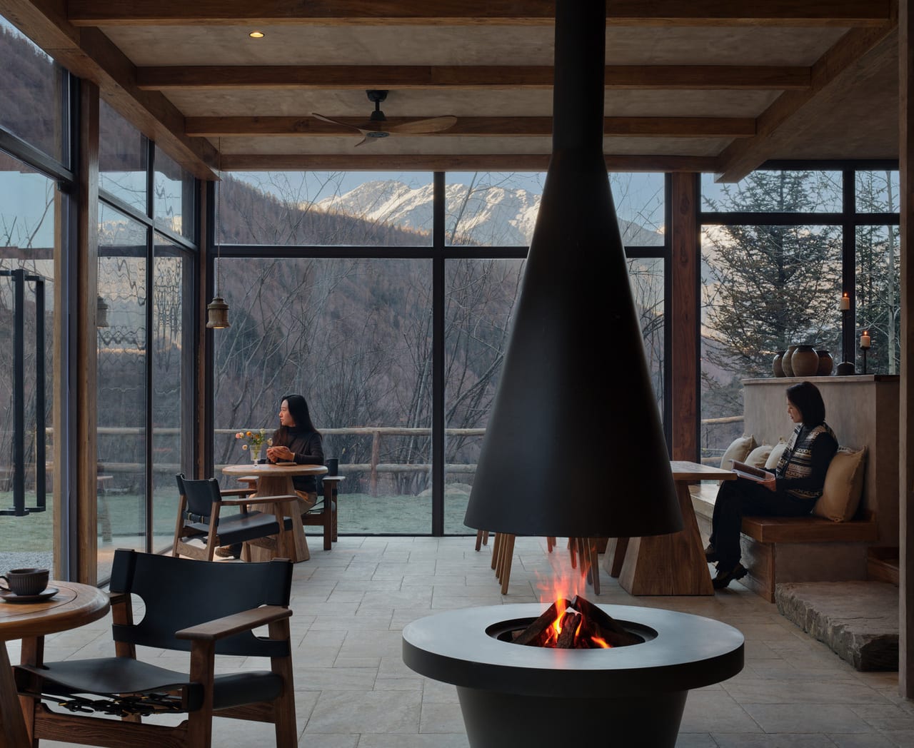Vacilando Siguniang — guest lounge built around a suspended-cone fireplace, glass walls onto the valley