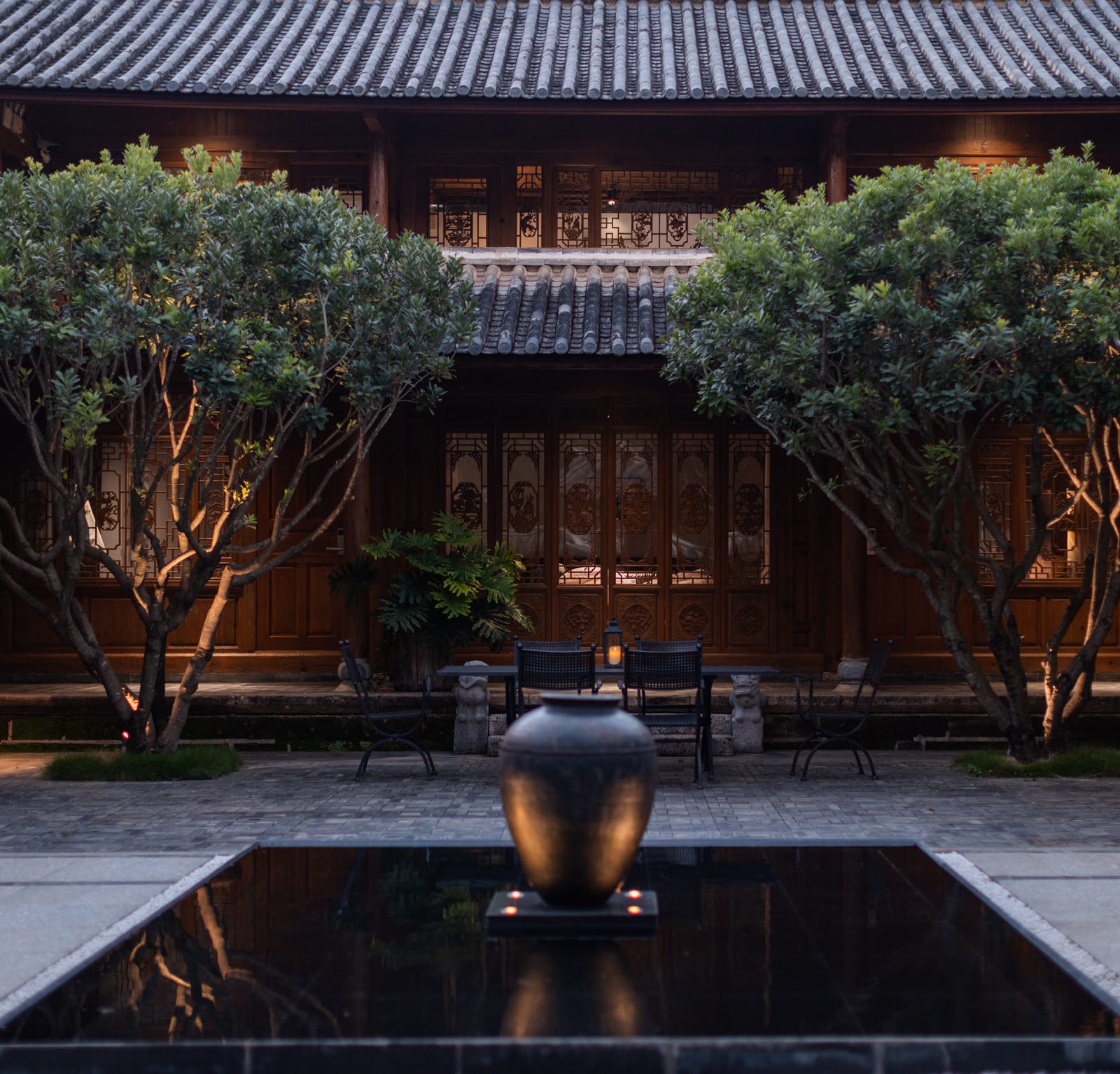 Wuliu Xinsu — carved timber doors across the courtyard, a clay jar at the head of the pool