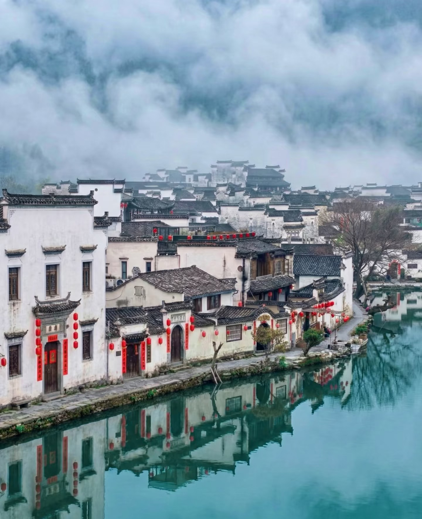 Hongcun's white walls and red lanterns reflected in the water, mist on the hills