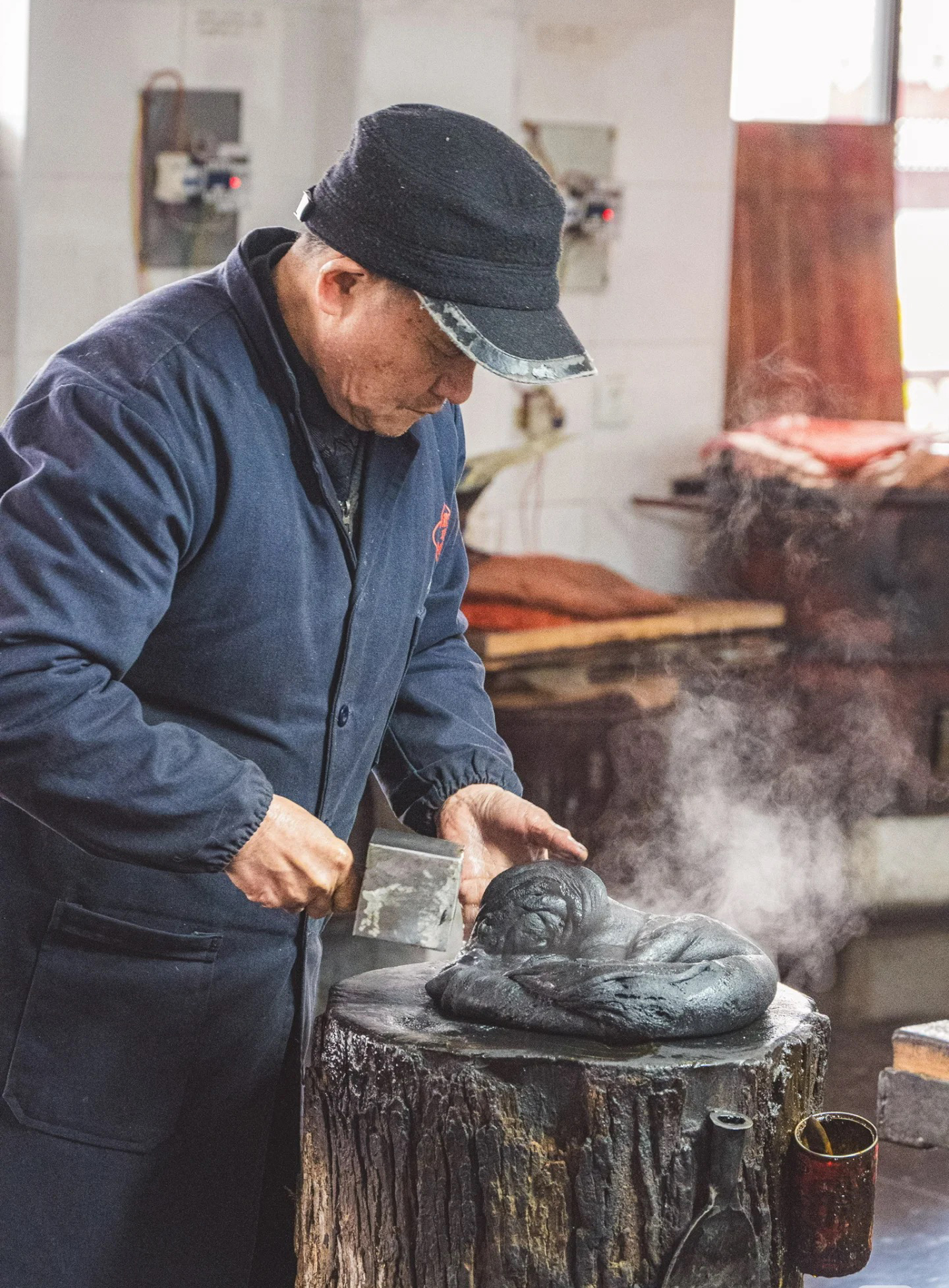 An ink-maker hammering a steaming block of ink paste on a tree-stump bench