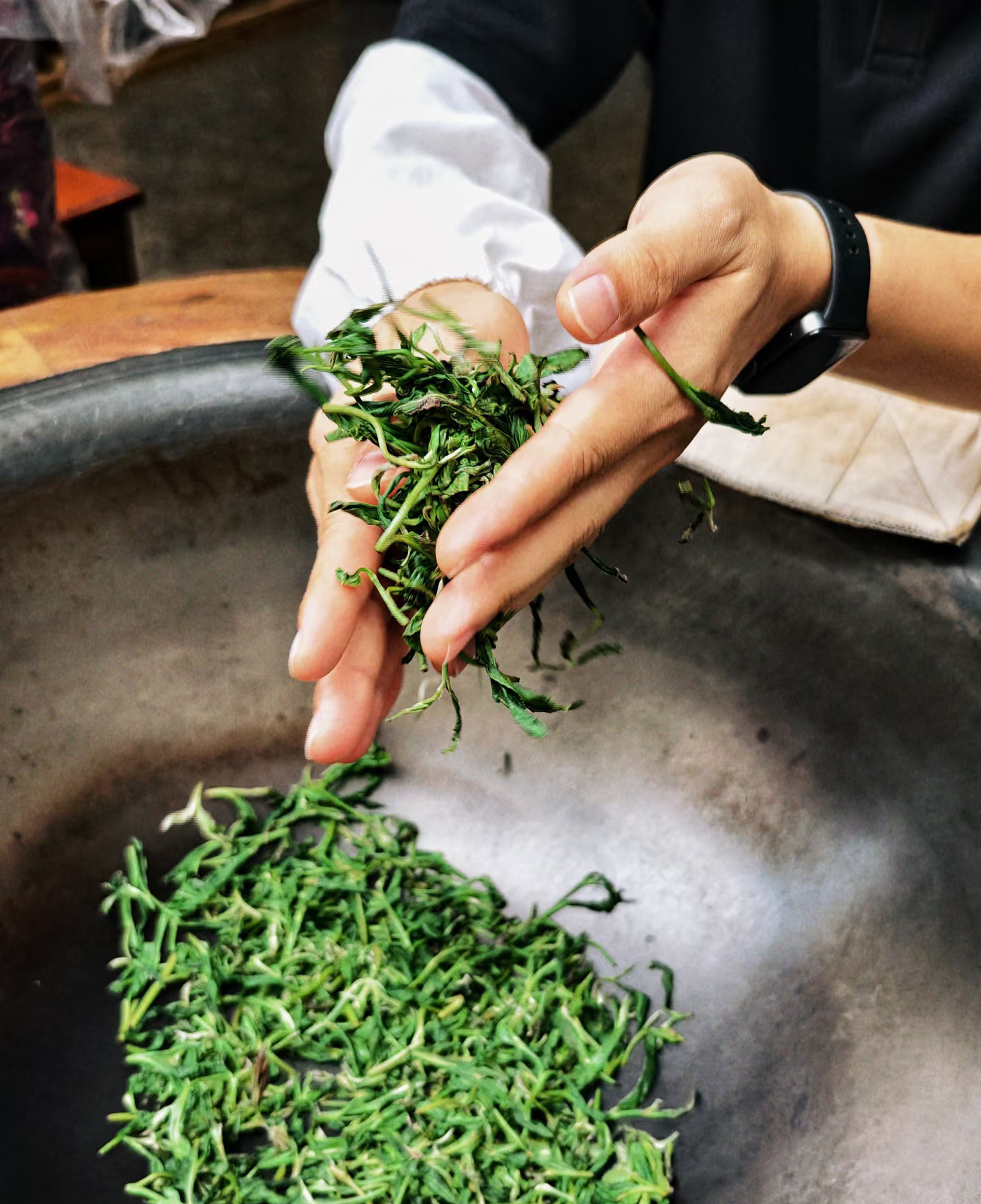 Hands turning fresh tea leaves in a hot wok