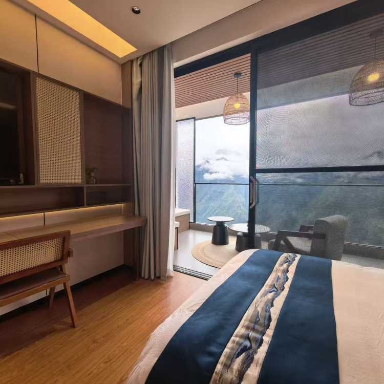 Shanjing Yungu — a king room in pale timber and rattan, glass onto the valley